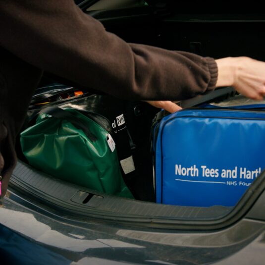 Hand of community nurse grabbing kitbag from car