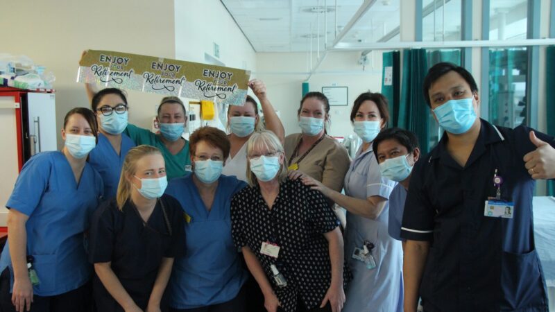 Ann Burton with her colleagues. Someone holds a banner reading "enjoy your retirement".