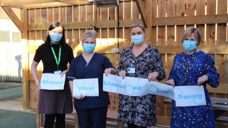 Jun Saw and some of her 100 Leaders pack. They hold signs reading: "#Cohort1 Virtual Education and Staff Training".