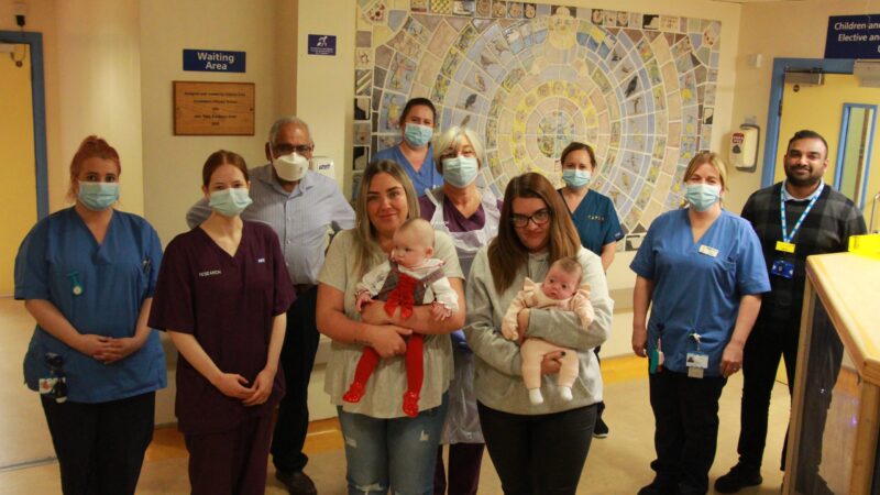 Babies participating in the study. They are being held by their mums. They stand with the research team.