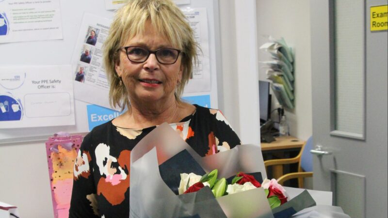 Marian Fleming stands in the ward. She holds a bunch of flowers.