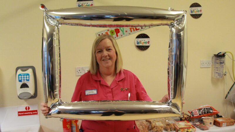 Clare wise stands in front of a buffet at her party. She holds a silver balloon photo frame around her head.