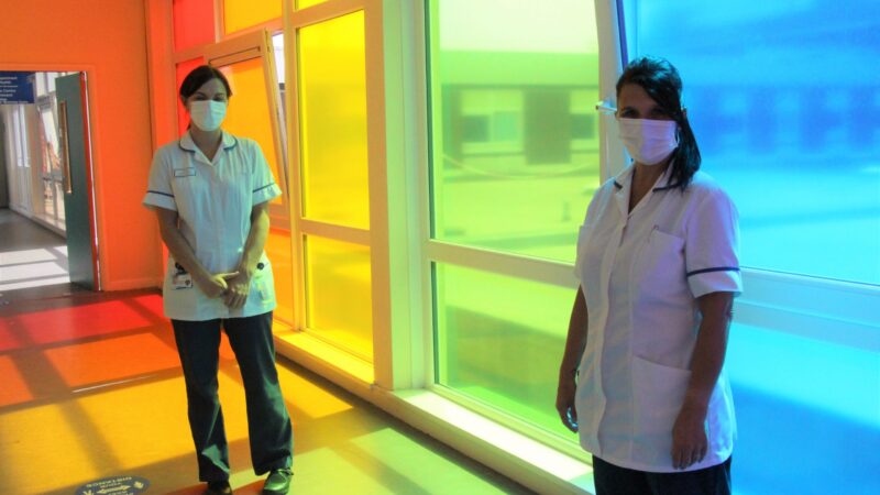 Gemma and Karen stand in a corridor.