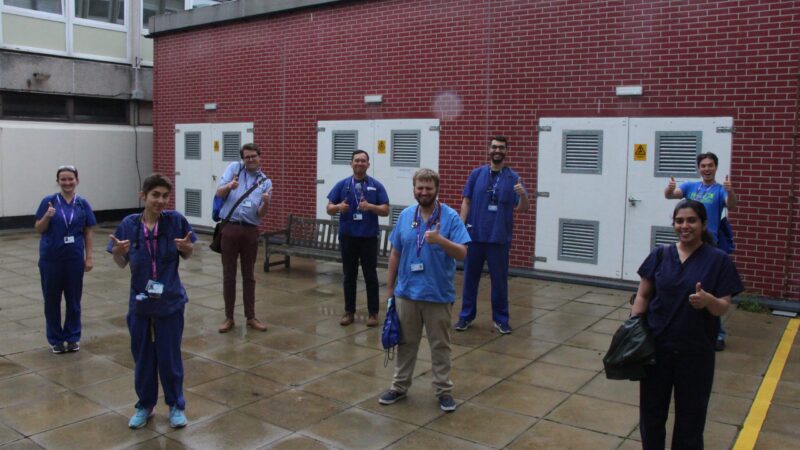 Medical trainees stand outside. They are all giving a thumbs up.