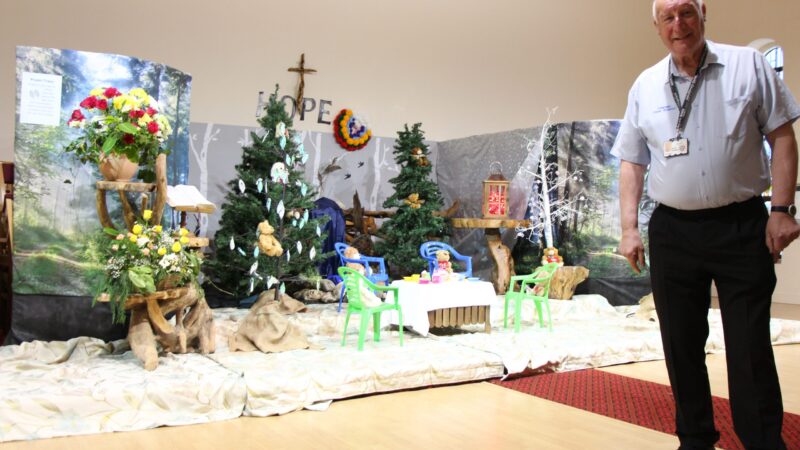 Dave Russon stands in front of the display. The display features a small table and chairs. Teddy bears sit on the chairs.