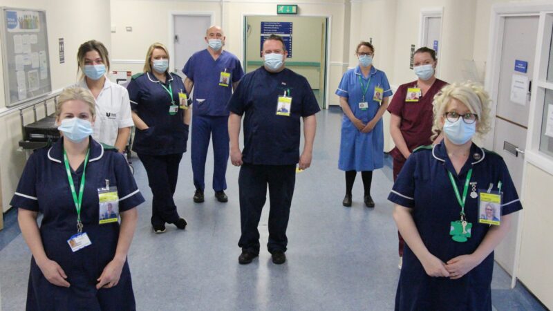 Staff wear their ID badges. They show a photo of themselves and read "#AndILookLikeThis". They all wear face masks.