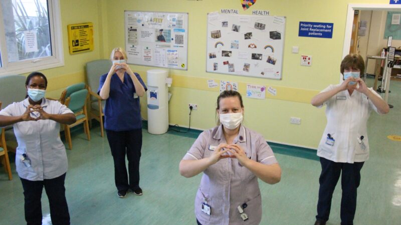 The centralised outpatients team stand in front of their display. They make hearts with their hands.