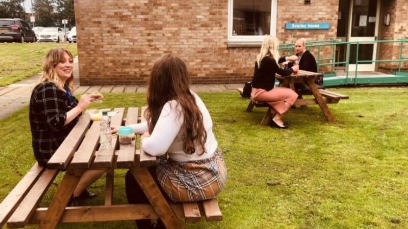 Staff sit at picnic benches.